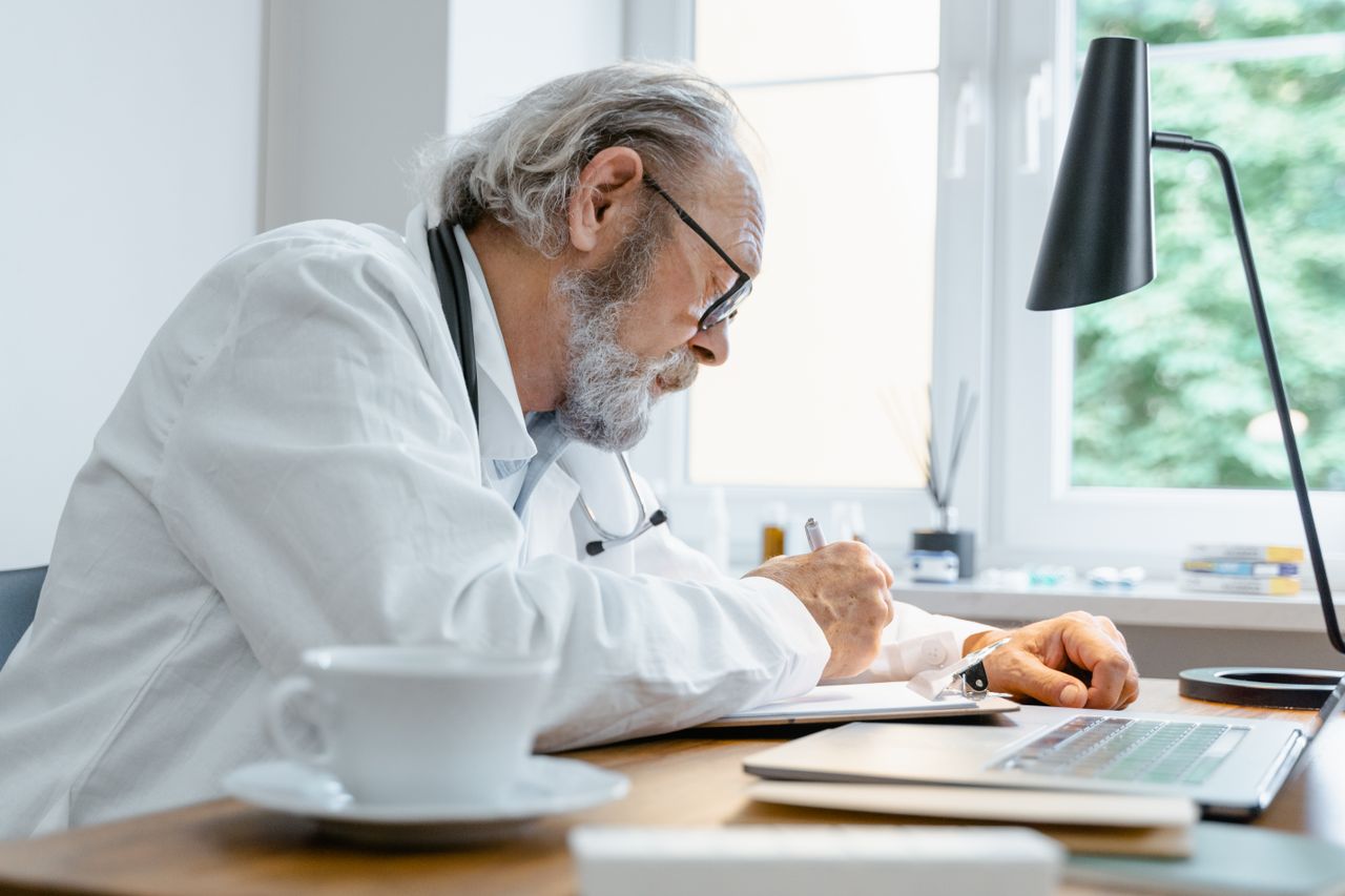 Physician in a white coat with a stethoscope, writing notes on medical records